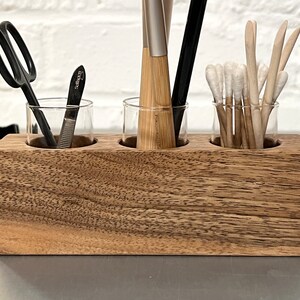 May include: A wooden organizer with three glass jars for holding small items. The jars are filled with various tools, including a pair of scissors, a nail file, and several thin wooden sticks.