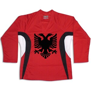 Puede incluir: Camiseta roja de manga larga con detalles en blanco y negro. La camiseta presenta un gr&aacute;fico de &aacute;guila bic&eacute;fala negra en la parte delantera.