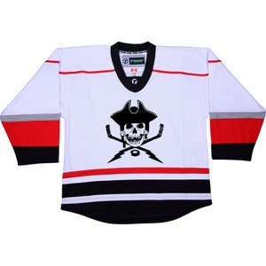 以下が含まれることがあります： 赤と黒のストライプが入った白いホッケーのジャージ。ジャージには、海賊の帽子をかぶった白黒のドクロとクロスボーンのグラフィックが描かれています。