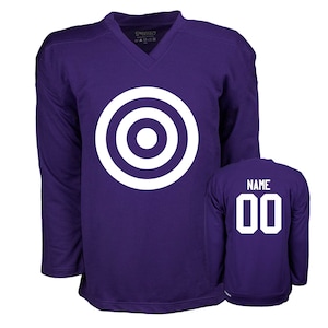 Puede incluir: Camiseta de hockey morada con un dise&ntilde;o de diana blanca en la parte delantera y el n&uacute;mero 00 en la parte trasera. La camiseta tiene cuello en V y mangas largas.