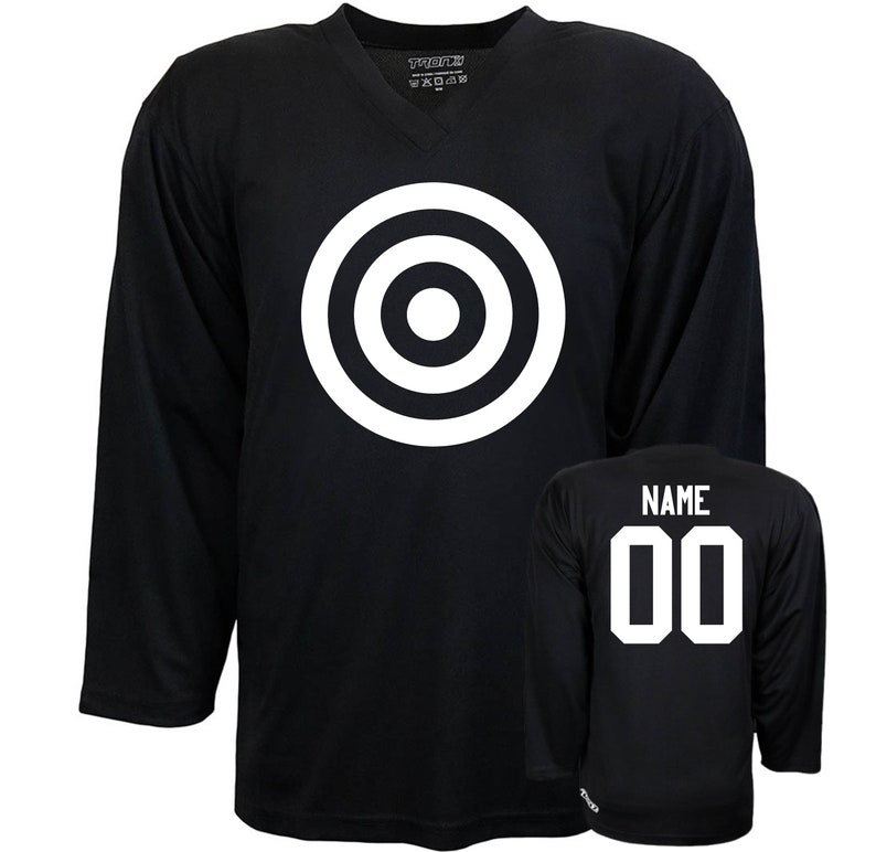 Puede incluir: Jersey de hockey negro con un dise&ntilde;o de diana blanco en la parte delantera y el n&uacute;mero "00" y la palabra "NAME" en la parte posterior.