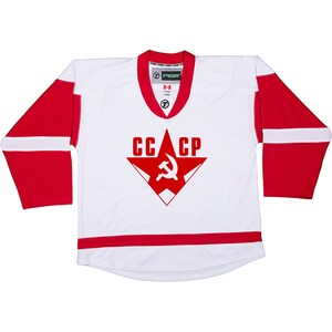 Puede incluir: Jersey de hockey blanco con rayas rojas y blancas. El jersey tiene una estrella roja con un martillo y una hoz dentro y el texto "CCCP" en la parte delantera.