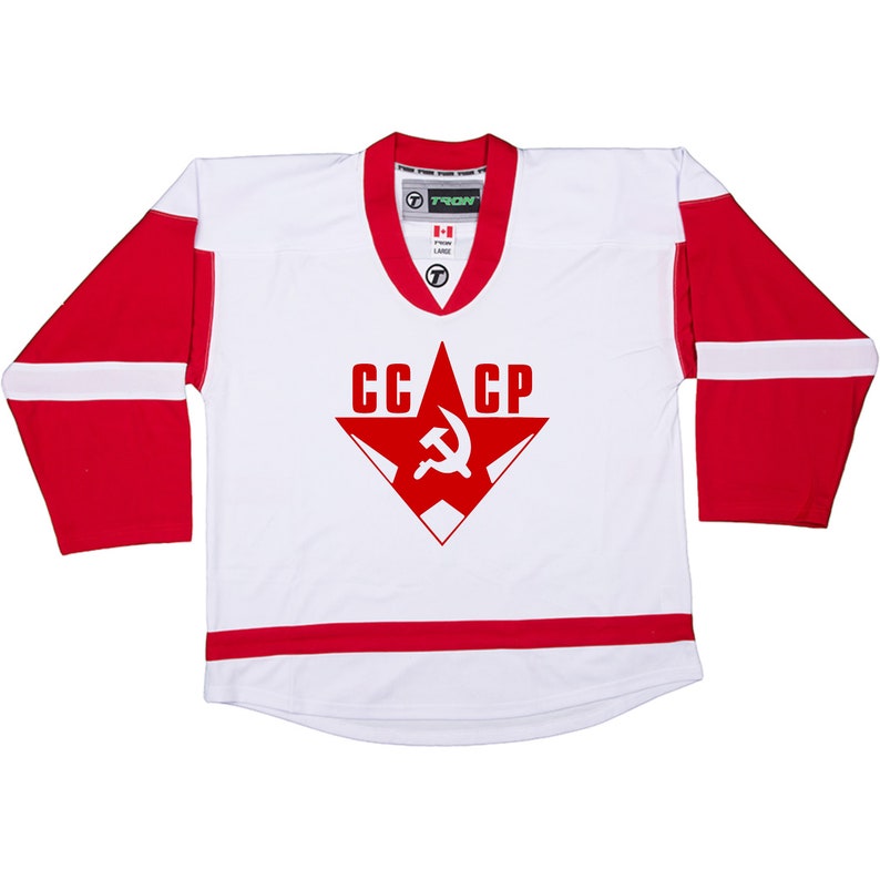 Puede incluir: Jersey de hockey blanco con rayas rojas y blancas. El jersey tiene una estrella roja con un martillo y una hoz dentro y el texto "CCCP" en la parte delantera.