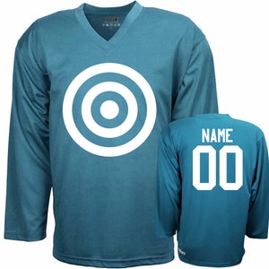 Puede incluir: Una camiseta de hockey azul turquesa con un dise&ntilde;o de diana blanca en la parte delantera y el texto "NAME 00" en la parte posterior.