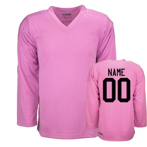 May include: Pink hockey jersey with long sleeves and a v-neck collar. The back of the jersey has the word "NAME" and the number "00" in black.