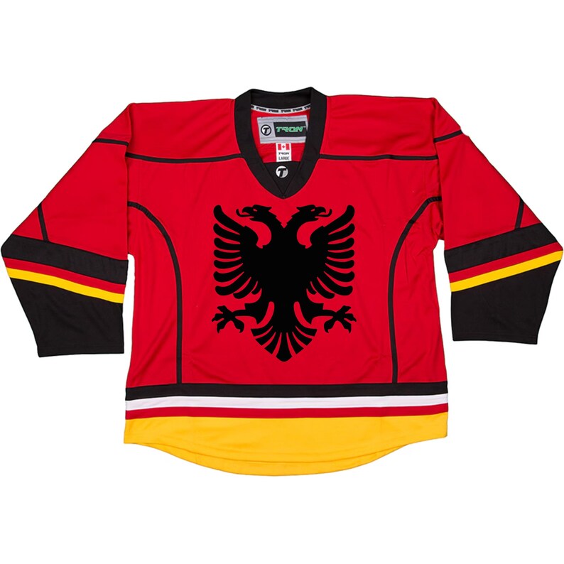Puede incluir: Jersey de hockey rojo y negro con el logotipo del &aacute;guila albanesa en la parte delantera. El jersey tiene rayas negras y amarillas en las mangas y una raya negra, blanca y amarilla en la parte inferior.