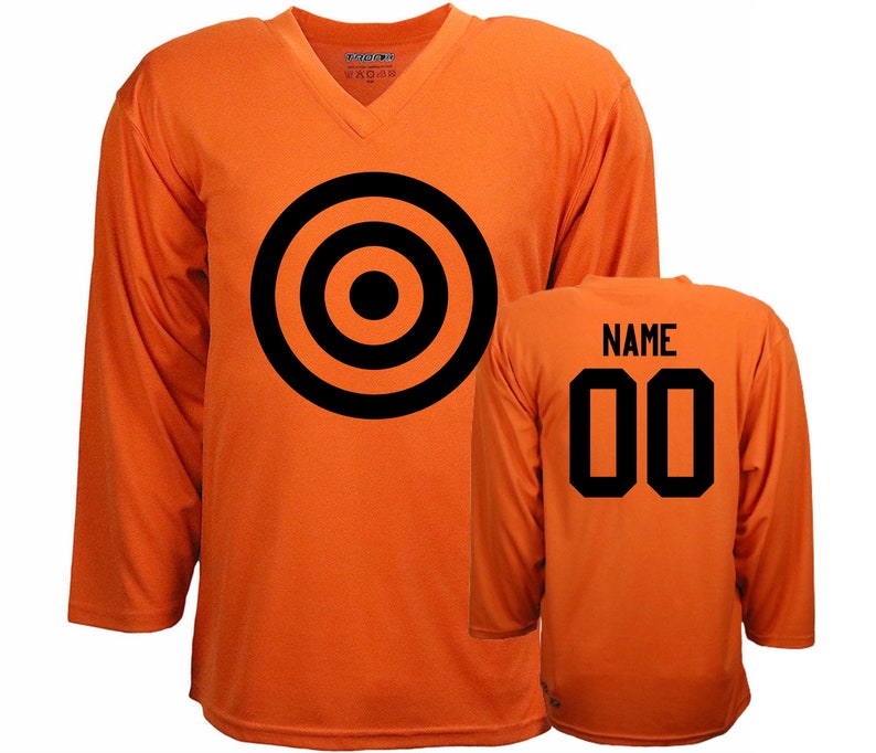 Puede incluir: Camiseta de hockey naranja con un dise&ntilde;o de diana negra en la parte delantera y el n&uacute;mero 00 y la palabra "NAME" en la parte trasera.