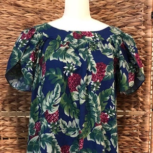 May include: A long, blue dress with a tropical leaf and berry pattern. The dress features short sleeves and a scoop neckline. The fabric is covered in large green leaves and red berry clusters. The dress is displayed on a mannequin.