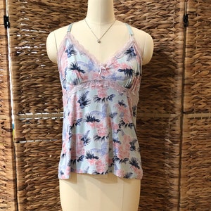 May include: A light blue camisole with a floral pattern of pink and blue flowers and leaves. The camisole has a lace trim around the neckline and straps. The garment is displayed on a mannequin.