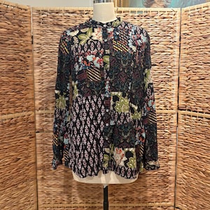 May include: A long-sleeved patchwork blouse with a mandarin collar. The blouse features a mix of floral, geometric, and abstract patterns in shades of black, red, green, and blue. The blouse is displayed on a mannequin.