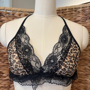 Könnte beinhalten: Ein Bralette mit Leopardenmuster und schwarzer Spitzenborte. Das Bralette hat ein Neckholder-Design und einen gewellten Spitzensaum am unteren Rand. Der BH wird auf einer Schaufensterpuppe präsentiert.