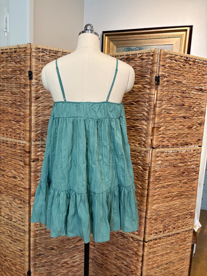 Op de afbeelding: Een teal-kleurige, gelaagde jurk met dunne spaghettibandjes. De jurk wordt getoond op een mannequin, waarbij de gerimpelde lagen en de textuur van de stof worden getoond. De jurk heeft een relaxte, vloeiende silhouet.