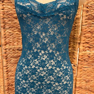 K&ouml;nnte beinhalten: Petrolfarbenes Spitzen-Slip-Kleid mit Spaghettitr&auml;gern. Das Kleid hat ein Blumenmuster und einen Wasserfallausschnitt. Der Stoff ist halbtransparent und gibt den Blick auf die darunterliegende Form frei. Das Kleid wird auf einer Schaufensterpuppe pr&auml;sentiert.