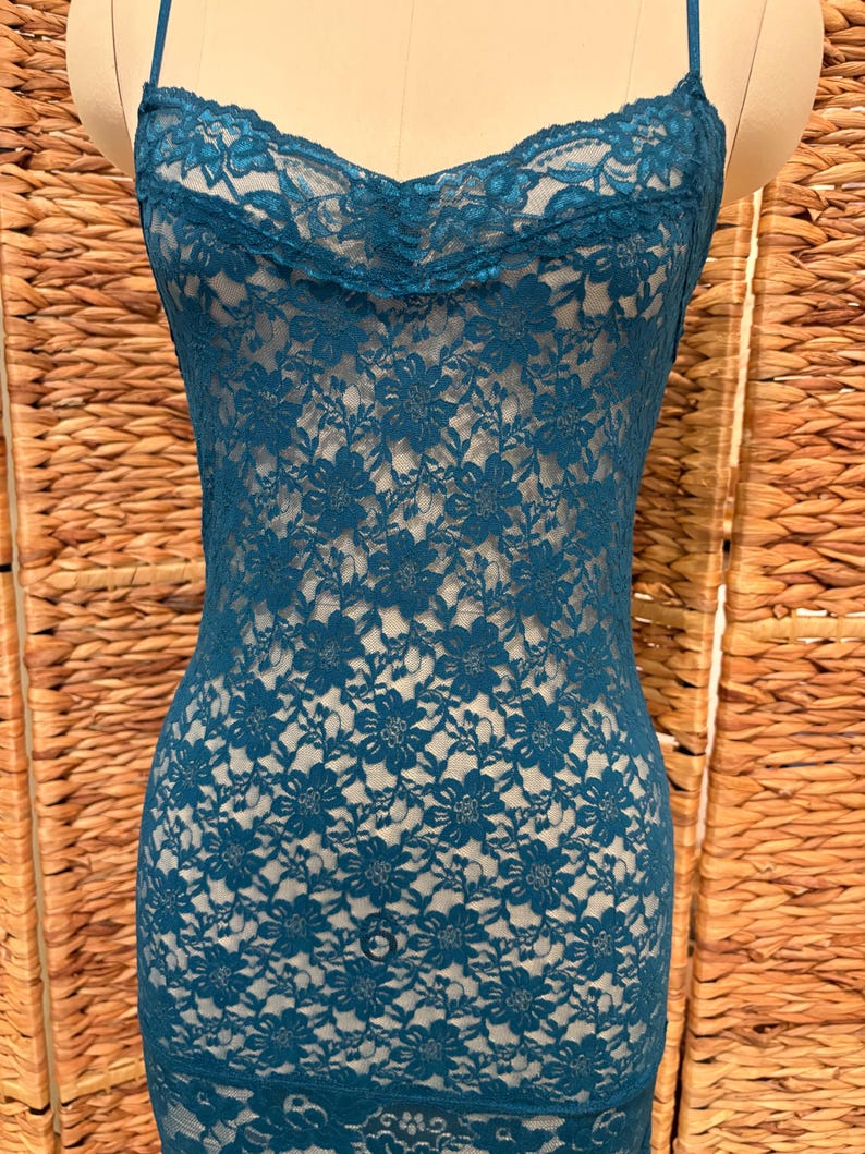 K&ouml;nnte beinhalten: Petrolfarbenes Spitzen-Slip-Kleid mit Spaghettitr&auml;gern. Das Kleid hat ein Blumenmuster und einen Wasserfallausschnitt. Der Stoff ist halbtransparent und gibt den Blick auf die darunterliegende Form frei. Das Kleid wird auf einer Schaufensterpuppe pr&auml;sentiert.