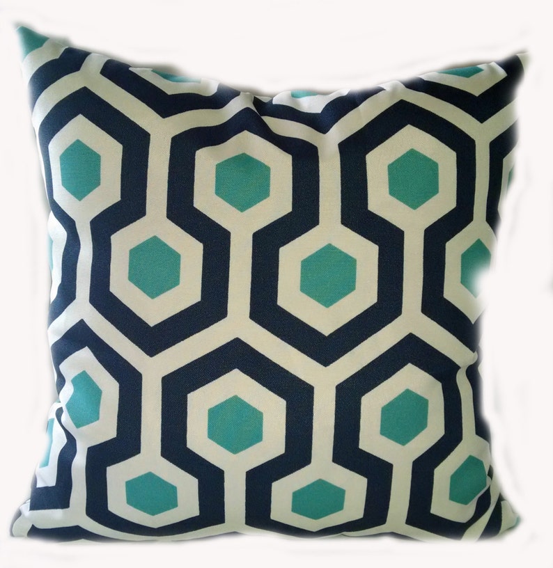 K&ouml;nnte beinhalten: Ein dekoratives Kissen mit einem geometrischen Muster in den Farben T&uuml;rkis, Wei&szlig; und Marineblau.