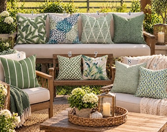May include: Nine square throw pillows arranged on outdoor furniture. Designs include green palm leaves, blue and white floral patterns, green geometric grids, solid green textures, white stripes, and green and blue abstract prints. Text reads RaindyDayDivine.