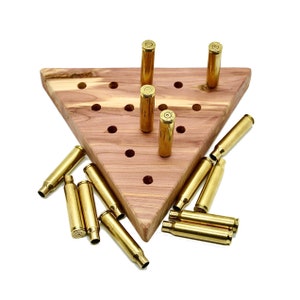 May include: A wooden triangular game board with holes and brass bullet casings. The casings are arranged in a pattern on the board and some are lying loose around the board.