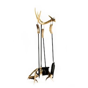 May include: A set of four fireplace tools with black metal handles and antler accents. The tools include a poker, a shovel, a brush, and tongs. The antler accents are attached to the handles with black leather straps.