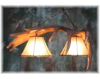 May include: A rustic chandelier made from two antler branches with two fabric lampshades. The chandelier is hanging from a chain.