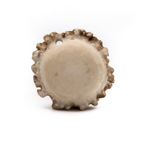 May include: A round, light brown antler button with a hole in the center. The button has a rough, textured surface.