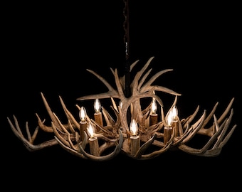 May include: A rustic antler chandelier with multiple light fixtures. The chandelier features a complex arrangement of antlers, with several candle-shaped bulbs providing warm illumination. The fixture is suspended from a chain against a black background.