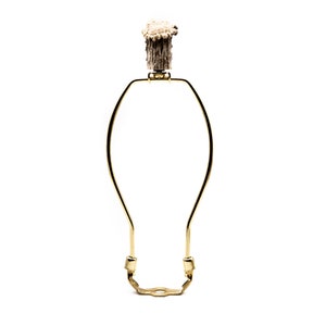 May include: A gold-colored lamp harp with a decorative antler finial. The finial is brown and cream-colored. The harp is designed to hold a lampshade and is made of a sturdy metal.