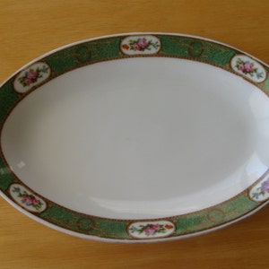 May include: White oval serving dish with a green and gold floral border. The border features pink and white flowers with green leaves.