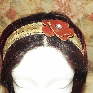 May include: A brown leather headband with a gold snakeskin pattern and a red leather flower with a rhinestone center.