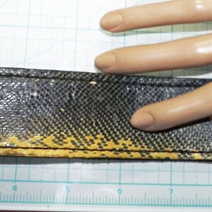 May include: A black and yellow leather bracelet with a textured pattern and two silver metal snaps. The bracelet is about 7 inches long.