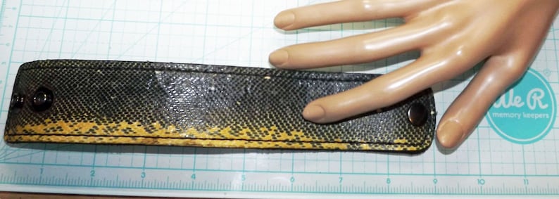 May include: A black and yellow leather bracelet with a textured pattern and two silver metal snaps. The bracelet is about 7 inches long.