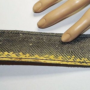 May include: A black and yellow leather bracelet with metal accents. The bracelet is made from recycled tire inner tube material.