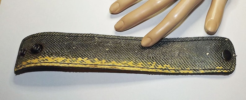 May include: A black and yellow leather bracelet with metal accents. The bracelet is made from recycled tire inner tube material.