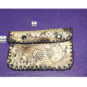 May include: A small, rectangular wallet made from snakeskin, measuring 5 inches wide and 3 inches long when closed. The wallet features a natural color pattern with black stitching and two black snap closures.