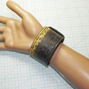 May include: A brown leather wrist cuff with a yellow snakeskin pattern.