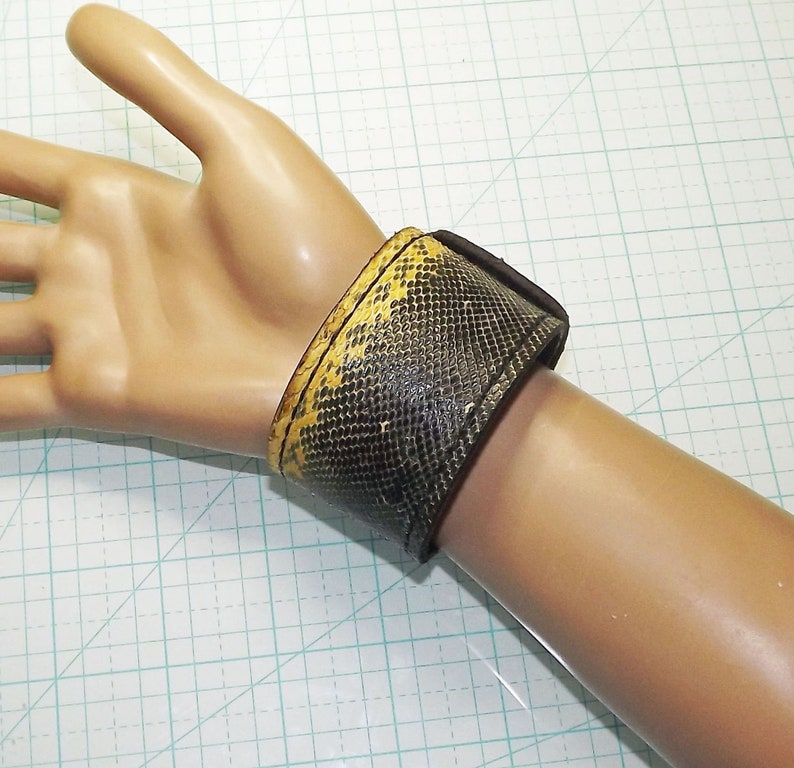 May include: A brown leather wrist cuff with a yellow snakeskin pattern.