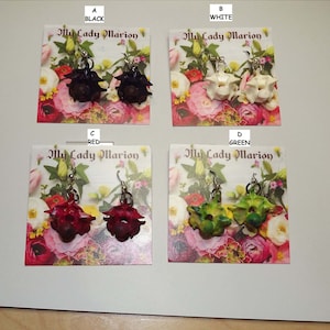 May include: Four pairs of handmade earrings in black, white, red, and green. Each pair features a unique, textured design. The earrings are displayed on cards with floral backgrounds and the text "My Lady Marion".