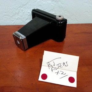 May include: A black vintage camera with a silver lens and a white note that says "Red Filters x2" with two red dots.