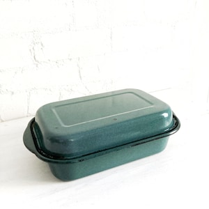 May include: A teal enamel loaf tin with a black rim and handles. The rectangular baking dish has a lid and is set against a white background. The vintage kitchenware is likely used for baking bread or other baked goods.