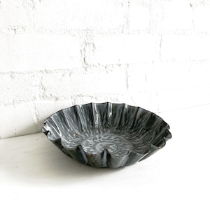 May include: A grey, fluted-edge bowl with a marbled pattern. The bowl is made of metal and sits on a white surface. The interior of the bowl has a lighter grey, swirling design.
