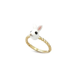 K&ouml;nnte beinhalten: Goldfarbener Ring mit einem wei&szlig;en Kaninchenkopf mit schwarzen Augen und rosa Innenohren. Das Ringband ist mit kleinen, goldfarbenen Perlen verziert. Auf dem Ringband steht "GOOD AFTERNOON".