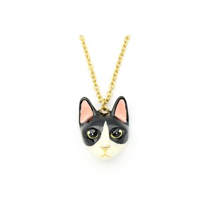May include: A gold chain necklace with a black and white enamel cat head pendant. The cat has pink ears and yellow eyes.