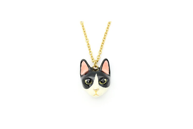 May include: A gold chain necklace with a black and white enamel cat head pendant. The cat has pink ears and yellow eyes.