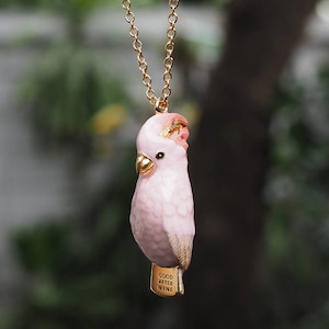 May include: A pink cockatoo bird charm necklace with a gold chain and the words "Good After Nine" on the charm.