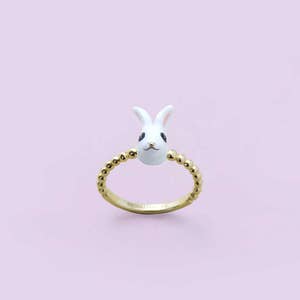 K&ouml;nnte beinhalten: Ein goldfarbener Ring mit einem wei&szlig;en Hasenkopf mit schwarzen Augen und rosa Ohren. Das Ringband ist mit kleinen, goldfarbenen Perlen verziert. Der Hintergrund ist helllila.