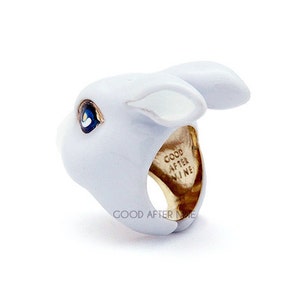 May include: A white ceramic rabbit ring with a gold band. The ring is inscribed with the words "Good After Nine".