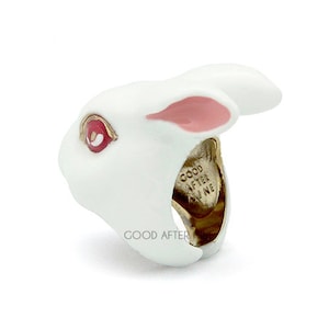 May include: White rabbit ring with pink ears and red eyes. The ring is made of metal and has the words "Good After Nine" inscribed on the band.