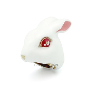 May include: White ceramic rabbit figurine with red eyes and pink ears. The rabbit's mouth is open and its teeth are visible.