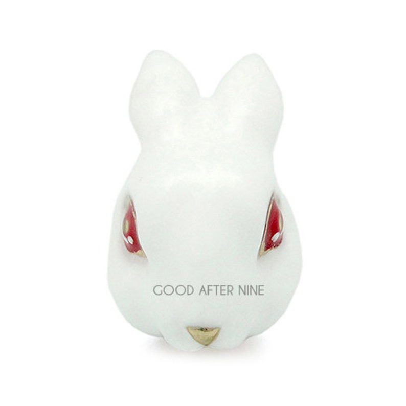 May include: White ceramic rabbit figurine with red eyes and gold accents. The rabbit's nose is pointed and its ears are long and floppy. The figurine is a good size for a shelf or desk.