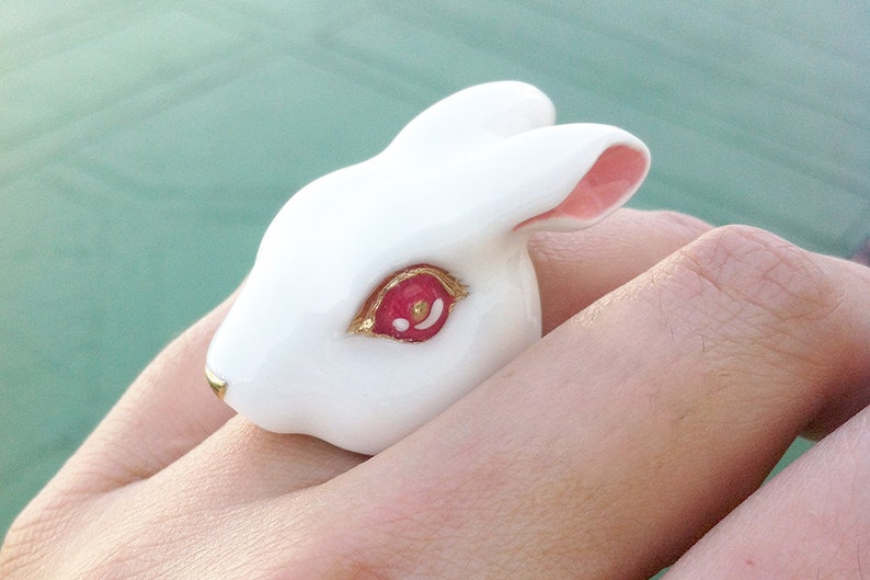 May include: White porcelain rabbit ring with a pink ear and a red eye with gold accents.