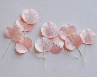 May include: A collection of peach-colored silk flower petals with thin wire stems. The petals are arranged on a white surface.